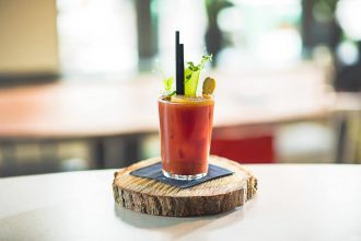 bloody mary cocktail with straw and garnishes, served on a wooden coaster