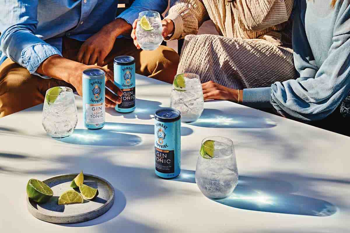 People around a table holding cans of Bombay Sapphire Canned Gin & Tonic