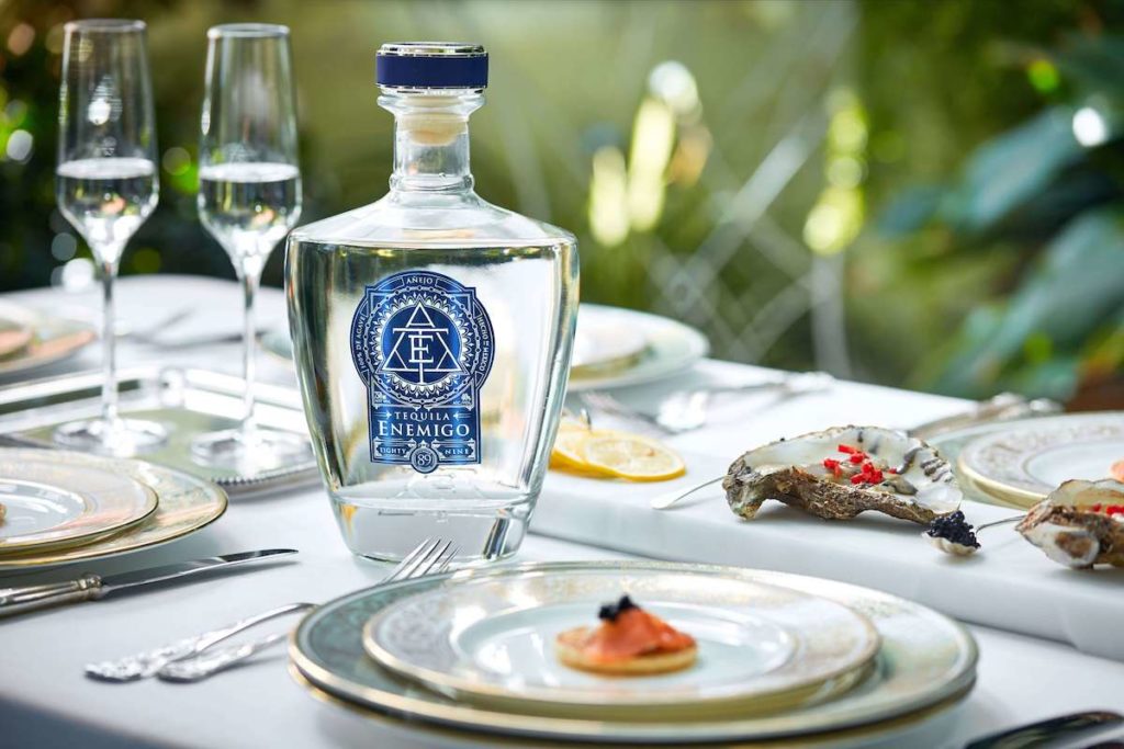 Tequila Enemigo Añejo Cristalino bottle on a table with plates and food