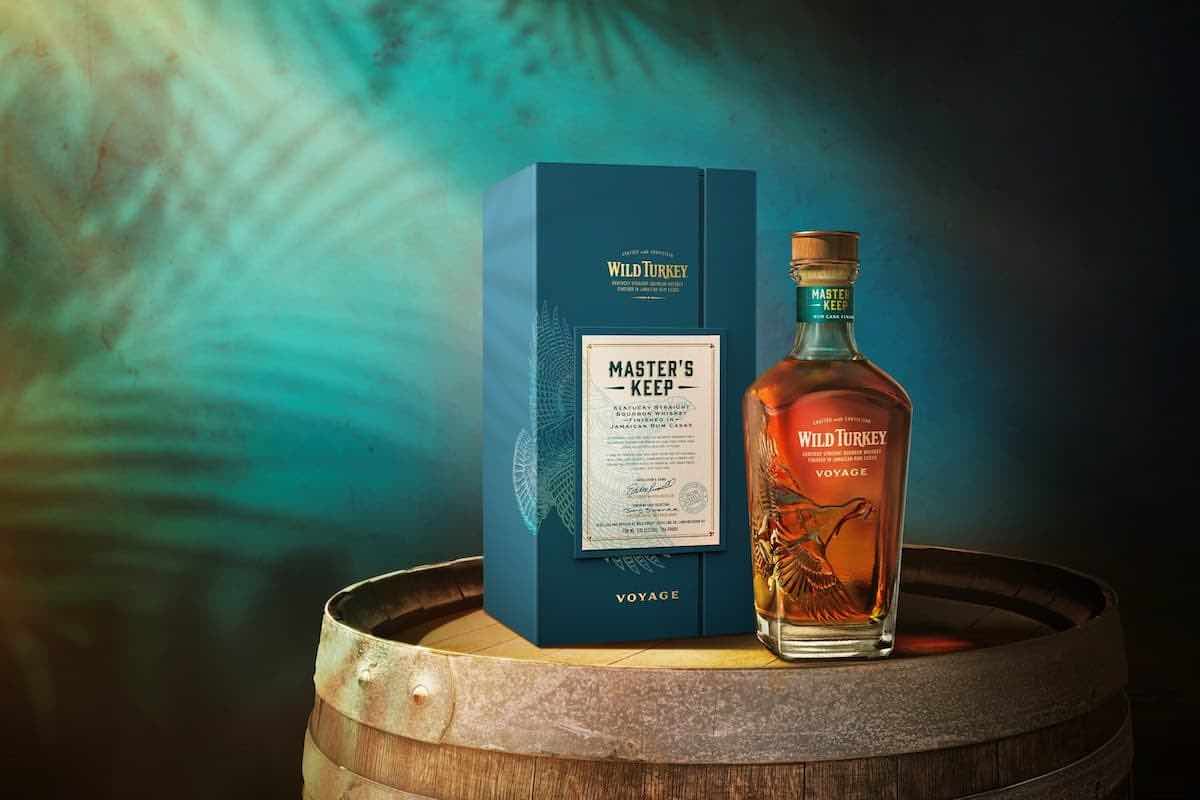 a bottle of wild turkey master's keep voyage bourbon on a wooden barrel