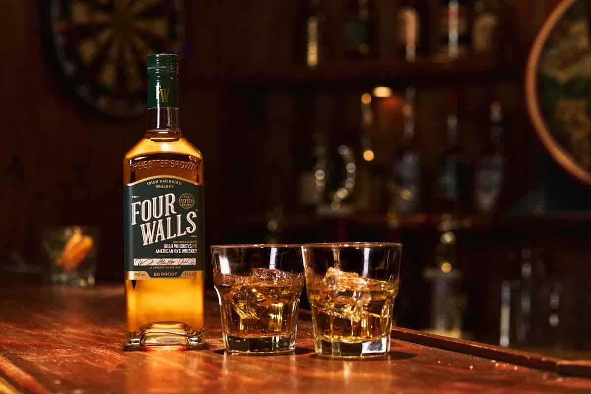 a bottle of four walls irish american whiskey with two glasses on a bar